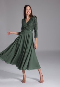 Robe longue verte avec un corsage en dentelle ajusté et des manches trois-quarts, présentant un col festonné et une jupe en satin fluide.