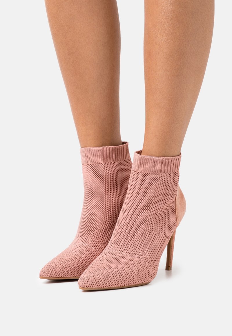 Stivali alla caviglia rosa con tomaia in maglia testurizzata e punta affilata, caratterizzati da un elegante tacco a spillo e un polsino a coste nella parte superiore.
