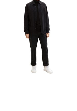 Musta napillinen paita mustan pooloneuleen päällä, yhdistettynä mustiin housuihin ja valkoisiin tennareihin. Paidassa on kaksi etutaskua ja rento istuvuus.