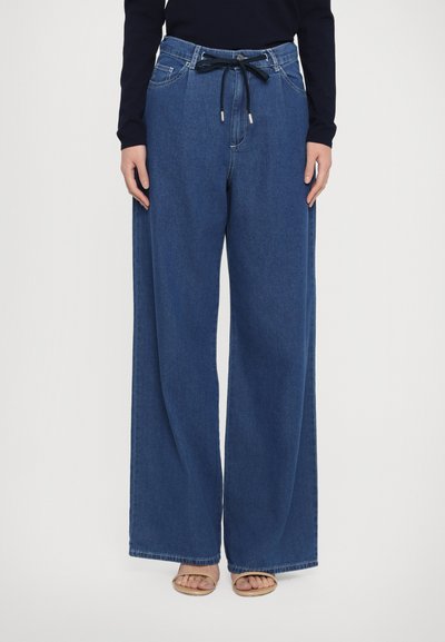 Bredde denimbukser i mørkeblå med snor i taljen, to frontlommer og diskrete syninger langs sømmene.