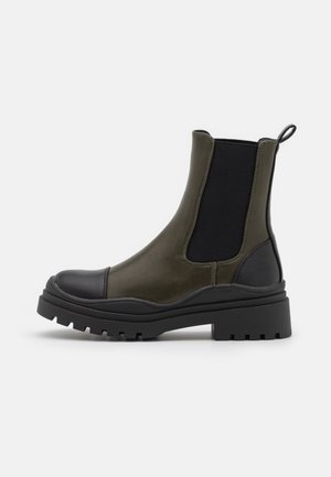 Bottines kaki avec des empiècements élastiques noirs sur les côtés, un bout arrondi et une semelle en caoutchouc noire épaisse avec un motif de crampons.