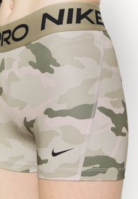 Close-up of person wearing beige and green camo Nike Pro compression shorts with black Nike swoosh and "NIKE PRO" waistband text.