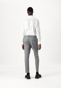 Hvit skjorte med en kontrasterende mørk krage, kombinert med lys grå slim-fit bukser. Svarte sko fullfører antrekket.