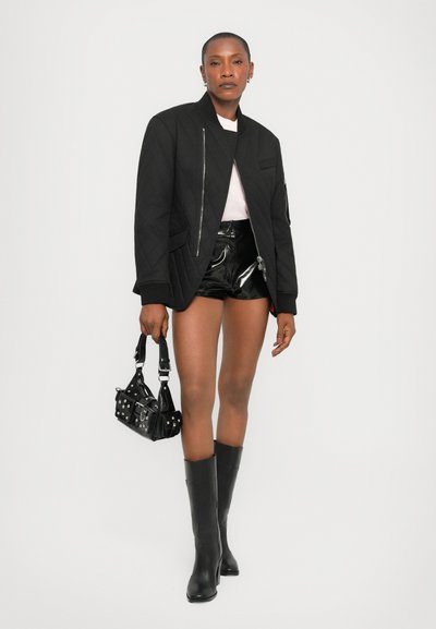 Giacca bomber nera trapuntata con chiusura a zip, top rosa, pantaloni corti neri in vernice, stivali neri fino al ginocchio e una piccola borsa nera con borchie.