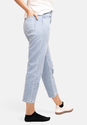 Jean en denim bleu clair avec une coupe droite, présentant une texture délavée, des poches arrière et des ourlets retournés, associés à des baskets et des chaussettes noires.