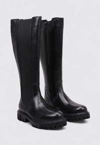 Bottes noires montantes en cuir avec une finition mate, dotées d'une fermeture éclair latérale, d'une semelle épaisse et de panneaux élastiques sur les côtés pour plus d'aisance.