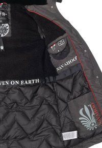 Schwarze Steppjacke mit einem Innenfutter aus Kunstfell, roten Akzentstichen, mehreren Taschen und gut sichtbarem Markenschild "NAVAHOO".