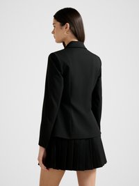 Μαύρο σακάκι με εφαρμοστή γραμμή, μακριά μανίκια και γιακά με εγκοπή, σε συνδυασμό με πλισέ μαύρη φούστα. Λεπτή υφή, κομψός σχεδιασμός.
