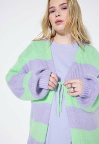 Strickjacke mit großen grünen und lavendelfarbenen Streifen. Sie hat lockere Ärmel und eine vorne offene, knopflose Gestaltung, die mit einem passenden Kordelzug zusammengehalten wird.