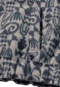 Fleece stof in lichtgrijs met donkergrijze abstracte patronen; heeft een zak en een golvende zoom langs de onderrand.
