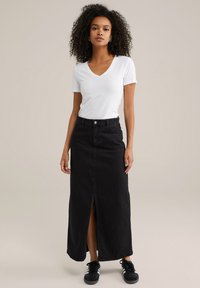 Črna jeans maxi krila s sprednjim razporkom, visokim pasom in gumbom za zapiranje, v kombinaciji z belo majico z V-izrezom in črnimi športnimi čevlji.