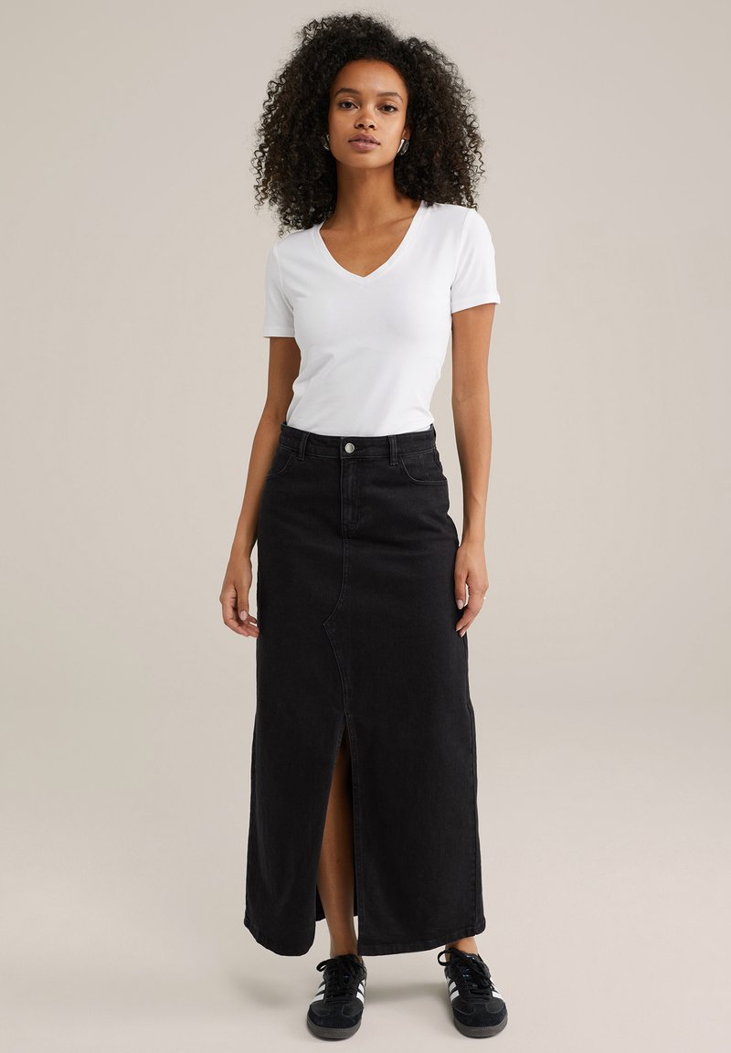 Črna jeans maxi krila s sprednjim razporkom, visokim pasom in gumbom za zapiranje, v kombinaciji z belo majico z V-izrezom in črnimi športnimi čevlji.