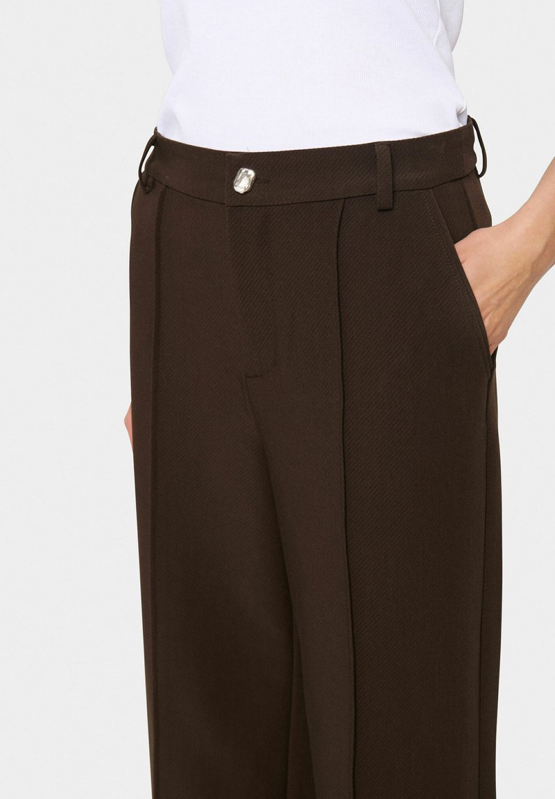 Brązowe dopasowane spodnie uszyte z teksturowanej tkaniny, z bocznymi kieszeniami i metalowym zapięciem na guzik, posiadające szlufki na pasek w talii.