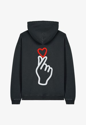 Musta kapuutsiga sviiter, millel on suur tikandiga graafika, kus käsi moodustab südamekuju, detailid valge ja punase niidiga. Loodud lõdva stiiliga ja tekstureeritud kangast.