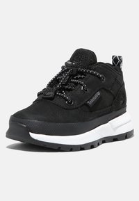 Black athletic shoe made of textured fabric with a sturdy rubber sole. Features elastic laces and a patterned pull tab at the heel.