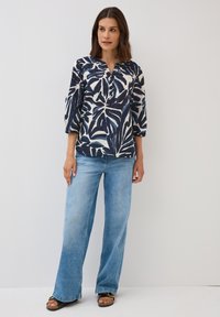 Blouse marine et crème avec un motif de feuilles, à manches trois-quarts, en V, associée à un jean large bleu clair et des sandales noires.