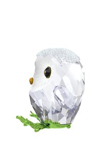 Figurína sovy z kryštálu s lesklým bielym telom, žltými akcentmi a textúrovanou srsťou. Umiestnená na základni z zelenej listu, vystavujúca zložitú fasetu.
