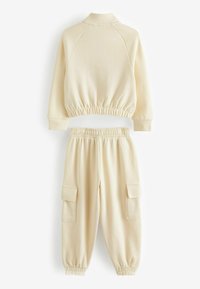 Kremfarvet træningsdragt bestående af en cropped sweatshirt med elastisk talje og matchende bukser med cargo-lommer og samlede mansjetter. Blød stoftekstur.