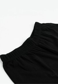 Fascia elastica nera su tessuto arricciato, probabilmente parte di un indumento, mostrata su uno sfondo bianco uniforme.