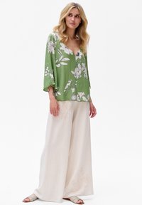 Zielona bluzka w kwiatowy wzór z dekoltem V i szerokimi rękawami, zestawiona z beżowymi spodniami typu wide-leg z delikatnymi haftowanymi detalami.
