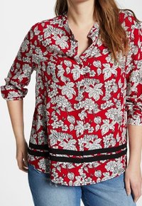 Camicia rossa a bottoni con motivi floreali bianchi di foglie e fiori, con accenti a strisce nere sull'orlo e maniche arrotolate.