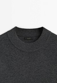 Pull gris foncé avec un col rond côtelé et une texture subtile. Le matériau semble doux et tricoté, avec une étiquette visible à l'intérieur du col.