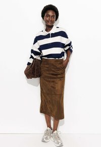 Polo rayé bleu marine et blanc à manches longues associé à une jupe midi en daim marron. Tenant un sac à main imprimé léopard et portant des baskets argentées.