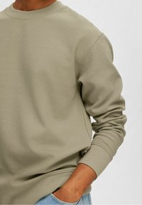 Světle olivově zelená mikina s texturovaným povrchem, kulatým výstřihem a dlouhými rukávy, doplněná světle modrými džíny. Pohodlný design.