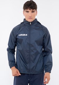 Giacca impermeabile blu navy con zip frontale, cappuccio regolabile, polsini elasticizzati e logo LEGEA in bianco sul petto.