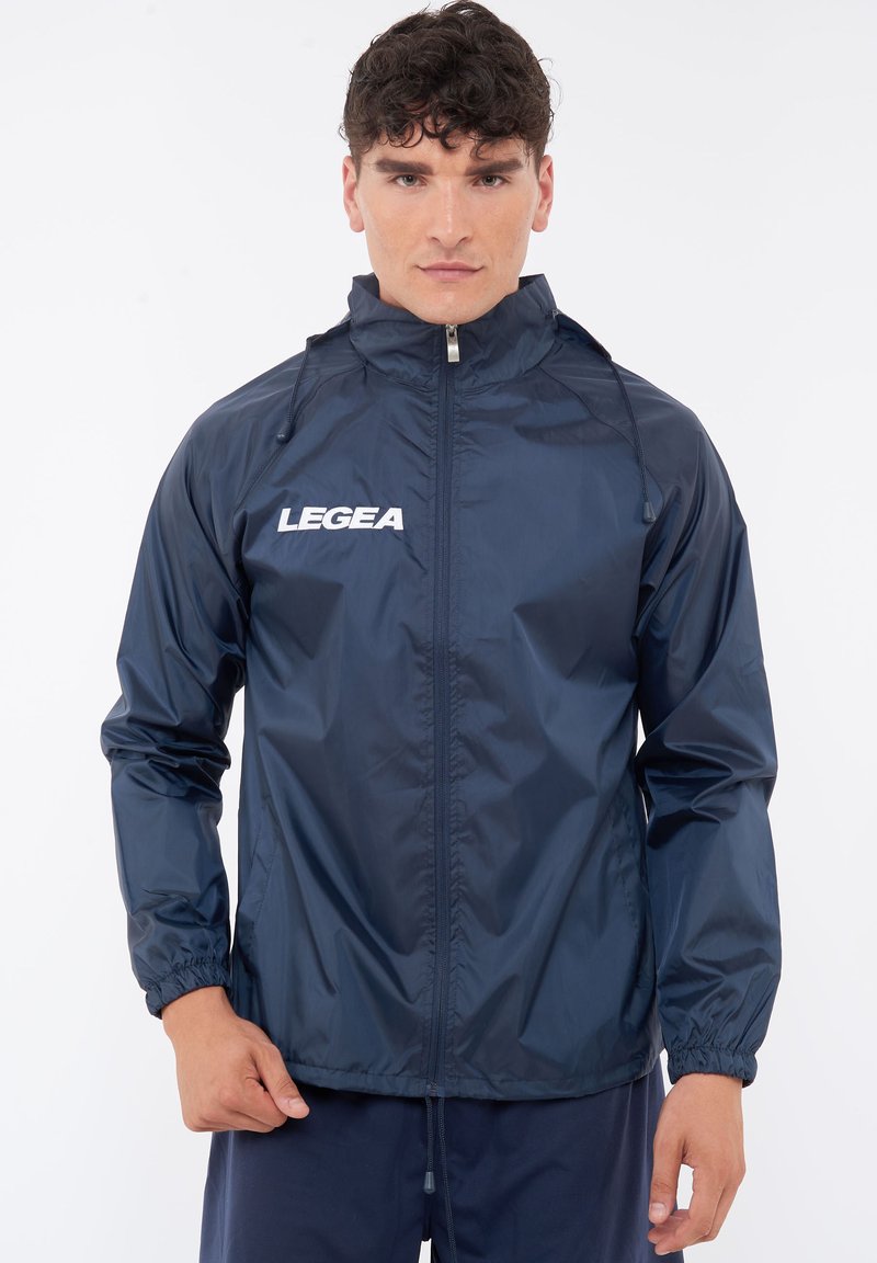 Giacca impermeabile blu navy con zip frontale, cappuccio regolabile, polsini elasticizzati e logo LEGEA in bianco sul petto.