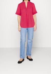 Blusa rossa a maniche corte con scollo a V e polsini ripiegati, abbinata a jeans azzurri chiari e ballerine nere. Design semplice con una vestibilità comoda.