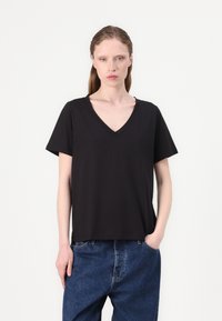 Black v-neck t-shirt made of soft fabric with short sleeves. Loose fit, plain design, no patterns or accents. Worn with blue denim pants.