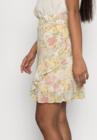 Blommig volangkjol i ljuskrämfärgad med rosa, gula och blå blommor. Har lager av volanger och en figurnära midja.