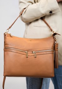 Sac à épaule en cuir tan avec deux poches zippées à l'avant, quincaillerie dorée et détail de pompon. Texture lisse et bandouillère ajustable.