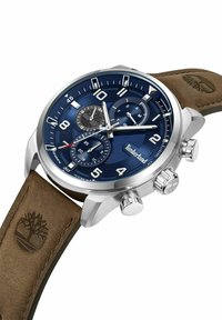 Hronogrāfa pulkstenis ar zilu ciparnīcu, sudraba nerūsējošā tērauda korpusu un brūnu ādas siksniņu ar reljefu logo. Trīs apakšciparnīcas un luminescējoši marķieri.