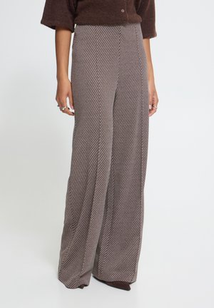 Femme portant un pantalon marron taille haute à jambes larges avec des rayures diagonales et un pull court marron foncé.