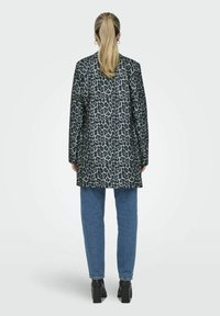Manteau long à imprimé léopard dans des tons de gris et noir, assorti à un jean en denim bleu et des bottes noires à talons. Tissu lisse avec des manches longues.