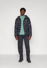 Jachetă puffer de culoare bleumarin cu fermoar și glugă, asortată cu un top cu guler de culoare verde mentă și pantaloni gri închis, având mansete elastice și buzunare.