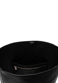 Grand sac cabas noir en cuir ouvert montrant un intérieur lisse avec une petite poche zippée et une étiquette de marque cousue à l'intérieur.
