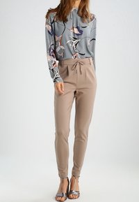 Langsleeve blouse met bloemenpatroon in grijs, gecombineerd met beige tapered broek en zilveren sandaaltjes met bandjes. Zachte textuur, casual fit.