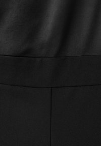 Gros plan sur un tissu noir montrant une couture de ceinture et des différences subtiles de texture entre deux sections de tissu.