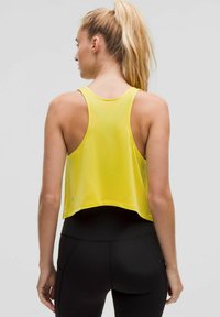 Geel crop tanktop, mouwloos, met een ronde halslijn en onafgewerkte randen. Draagt erbij een zwarte legging, met een gladde textuur en casual pasvorm.
