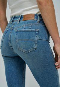 Jeans de mezclilla azul con un diseño ajustado, que cuentan con un parche de cuero de la marca Salsa Jeans en la cinturilla y dos bolsillos traseros.