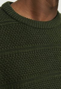 Pull en tricot vert olive avec un motif texturé, arborant un col rond à côtes et des détails en rayures horizontales.