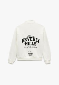 Biała bluza z nadrukiem "BEVERLY HILLS" w odważnym czarnym kolorze, z adresem w Kalifornii poniżej oraz napisem "GOOD VIBES" na dole. Gładka tekstura.