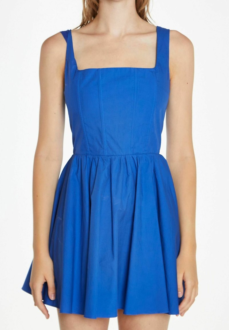 Femme portant une robe sans manches bleu vif cintrée, avec un col carré et une jupe froncée et évasée.