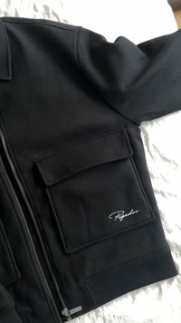 Czarna kurtka na zamek wykonana z miękkiego materiału, z dużą naszywaną kieszenią i ściągaczami na mankietach. Na kieszeni haftowany napis "Pegador".