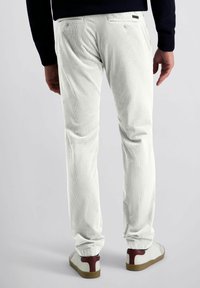 Witte, ribbelige corduroy broeken met een tapse pasvorm, voorzien van twee achterzakken en subtiele stikdetails. G gedragen met witte sneakers en bruine accenten.