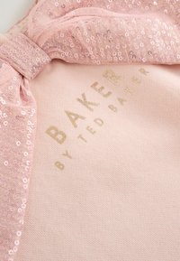Šviesiai rožinė medžiaga su sekančių pailleto dekoracijų sluoksniu ir kaspinu. "BAKER BY TED BAKER" išspausdinta auksinėmis raidėmis.