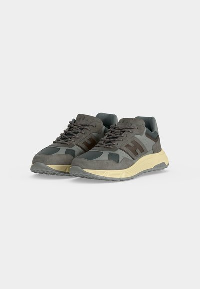 Paire de baskets athlétiques grises et vert foncé avec des semelles épaisses beiges et des lacets à motifs sur fond blanc.